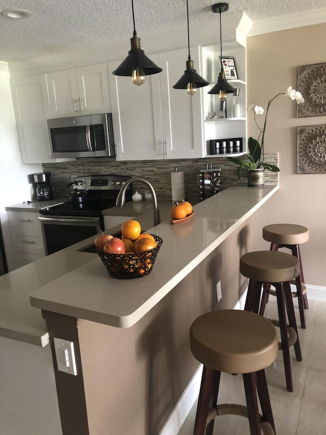 kitchen featuring a breakfast bar, crown molding, backsplash, appliances with stainless steel finishes, and a textured ceiling