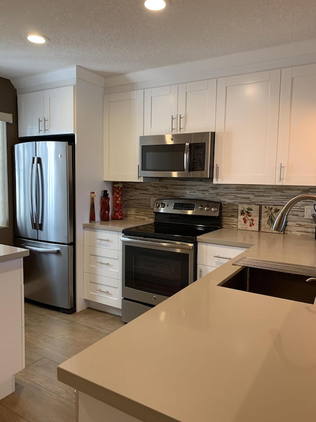 kitchen with light countertops, backsplash, appliances with stainless steel finishes, white cabinetry, and a sink