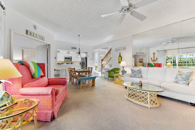 living area featuring ceiling fan, a textured ceiling, carpet floors, visible vents, and stairway