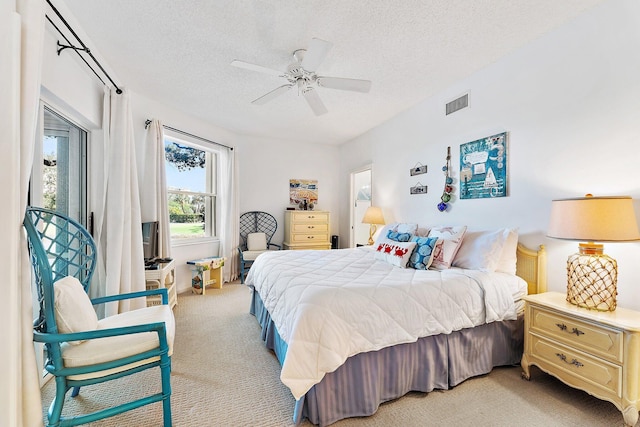 bedroom featuring light carpet, a textured ceiling, visible vents, and a ceiling fan