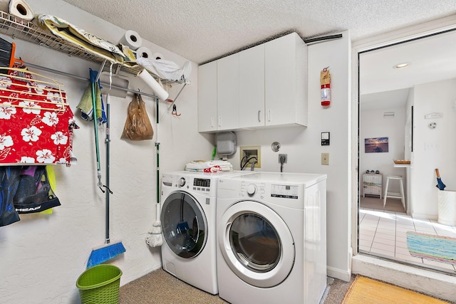 clothes washing area with a textured ceiling, separate washer and dryer, and cabinet space