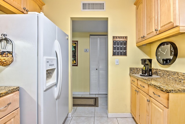 kitchen with white refrigerator with ice dispenser, visible vents, light stone countertops, light brown cabinetry, and light tile patterned flooring