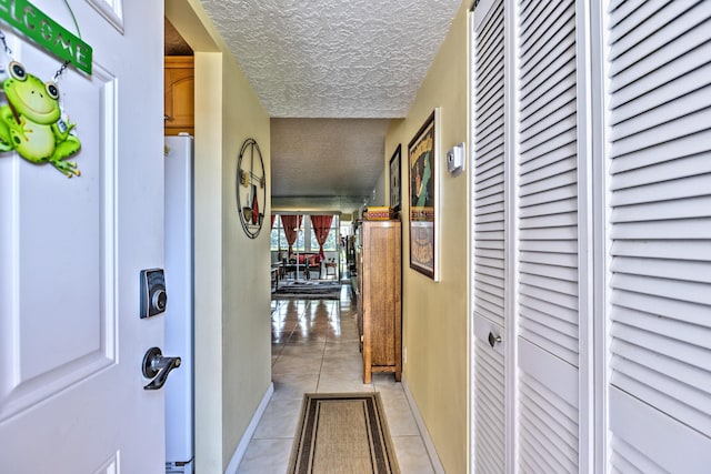 corridor featuring baseboards, a textured ceiling, and light tile patterned flooring