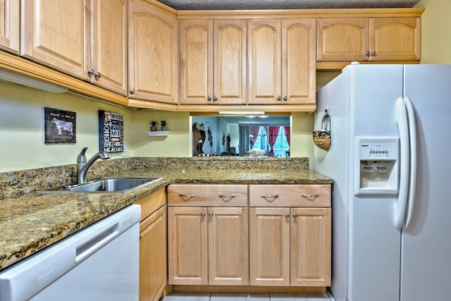 kitchen with stone counters, white appliances, light brown cabinets, and a sink