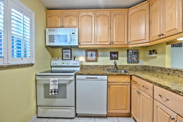 kitchen featuring light brown cabinets, white appliances, dark stone countertops, and a sink