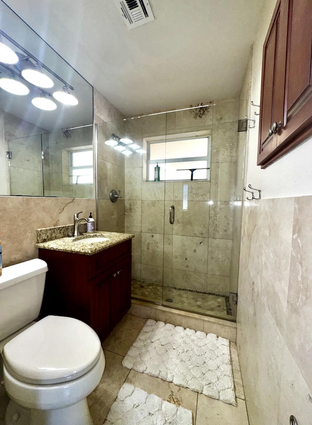 bathroom with visible vents, toilet, vanity, a shower stall, and tile walls