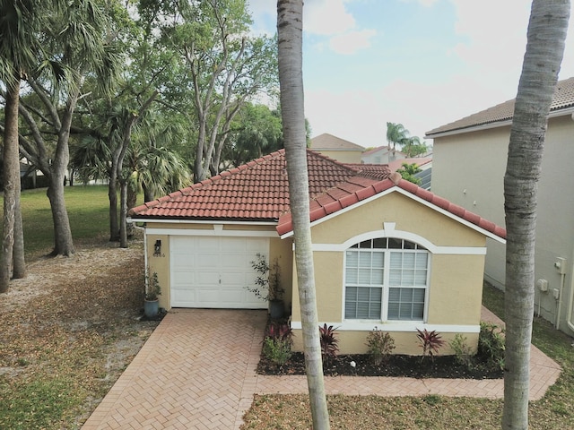 mediterranean / spanish house with a garage, a tiled roof, decorative driveway, and stucco siding