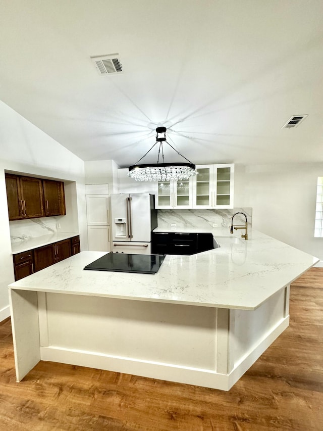 kitchen with black electric stovetop, white fridge with ice dispenser, visible vents, and wood finished floors