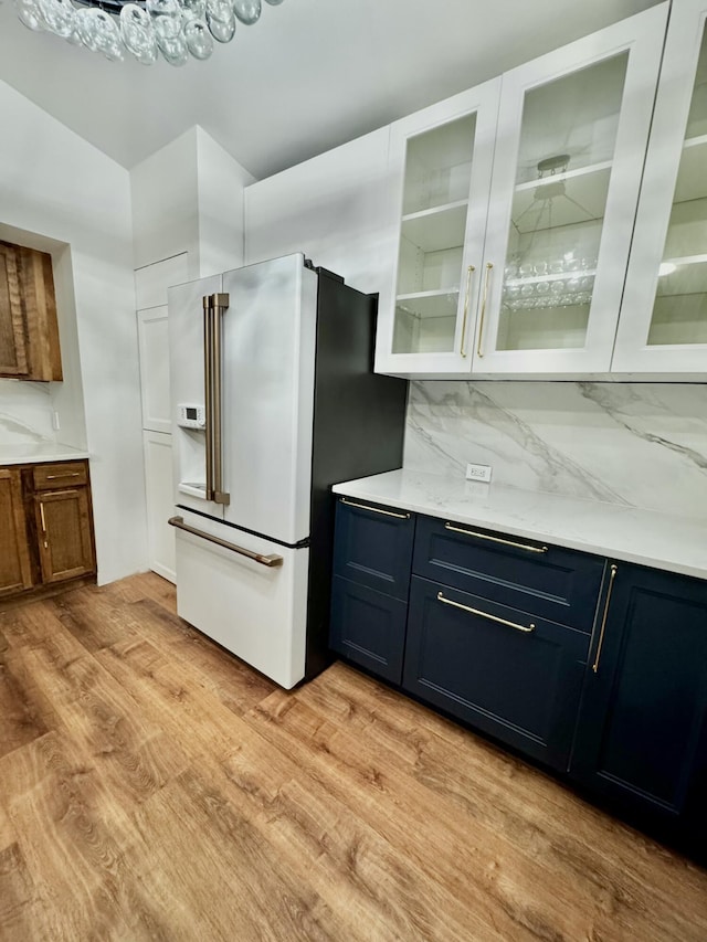 kitchen with high end fridge, light countertops, light wood-type flooring, backsplash, and glass insert cabinets