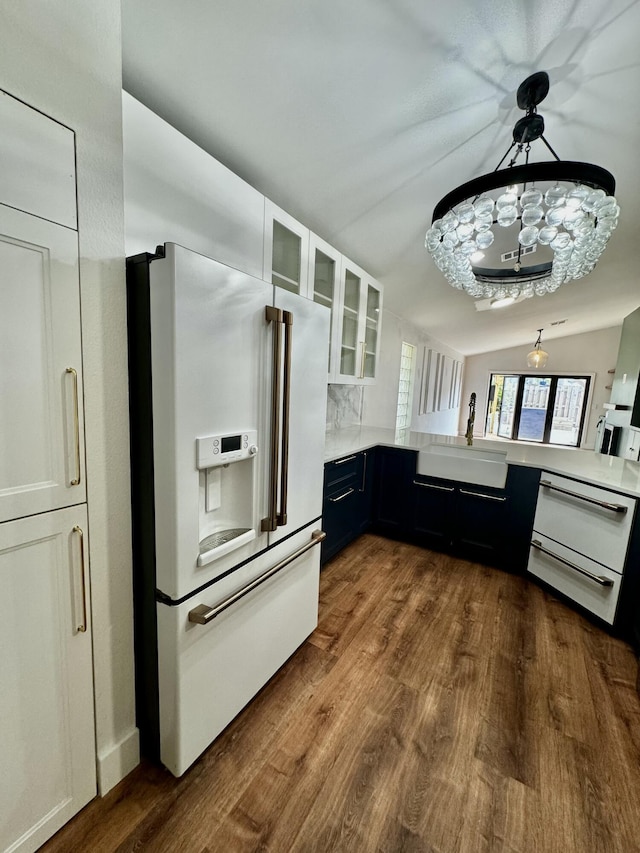 kitchen with high end white refrigerator, white cabinets, dark wood-style floors, glass insert cabinets, and a sink