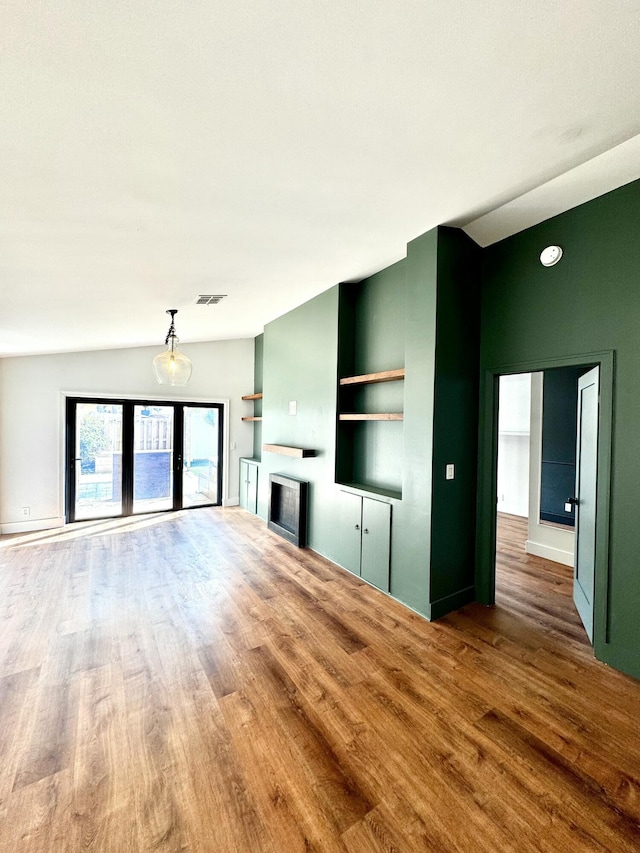 unfurnished living room featuring lofted ceiling, a fireplace, visible vents, and wood finished floors