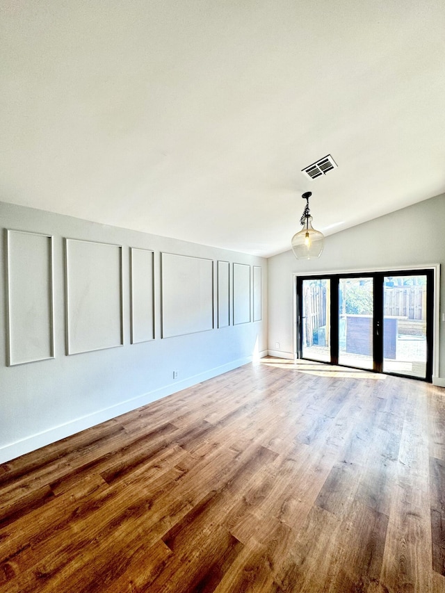 empty room featuring lofted ceiling, wood finished floors, visible vents, and a decorative wall