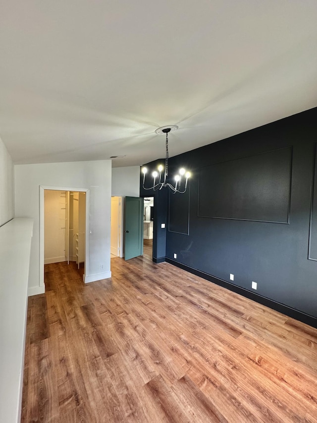 unfurnished dining area with baseboards, an inviting chandelier, and wood finished floors