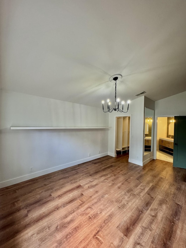 unfurnished dining area featuring baseboards, visible vents, a chandelier, and wood finished floors