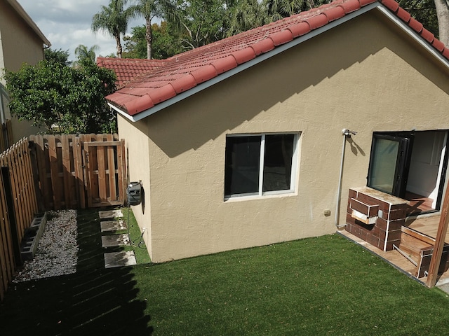 view of side of property featuring a lawn, fence, a tile roof, and stucco siding