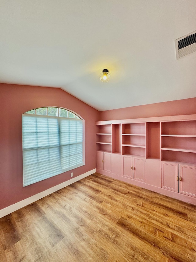 interior space featuring light wood-style floors, lofted ceiling, visible vents, and baseboards