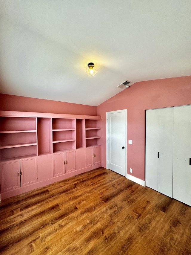 unfurnished bedroom featuring a closet, visible vents, vaulted ceiling, wood finished floors, and baseboards