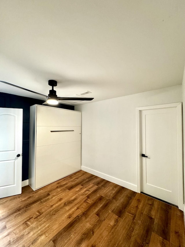 unfurnished bedroom with dark wood-style flooring, a ceiling fan, and baseboards