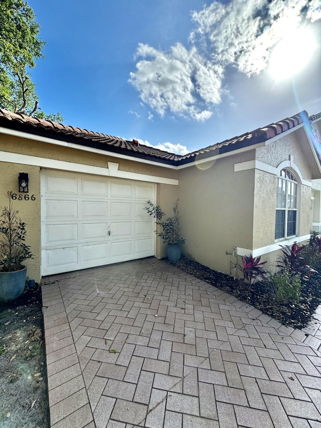 view of side of home featuring a garage, decorative driveway, and stucco siding