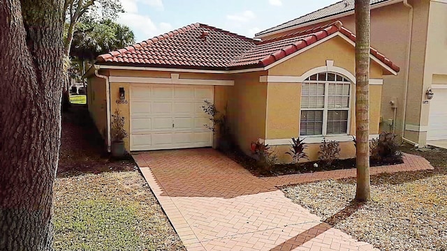 view of front of home featuring an attached garage, a tiled roof, decorative driveway, and stucco siding