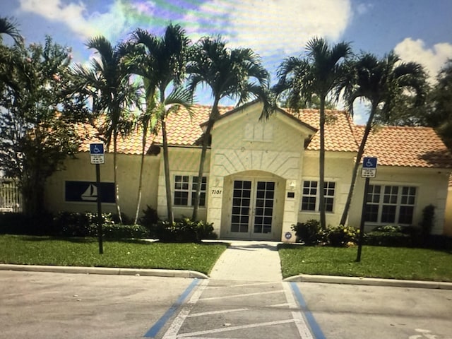 mediterranean / spanish-style house featuring a tiled roof, french doors, a front lawn, and stucco siding