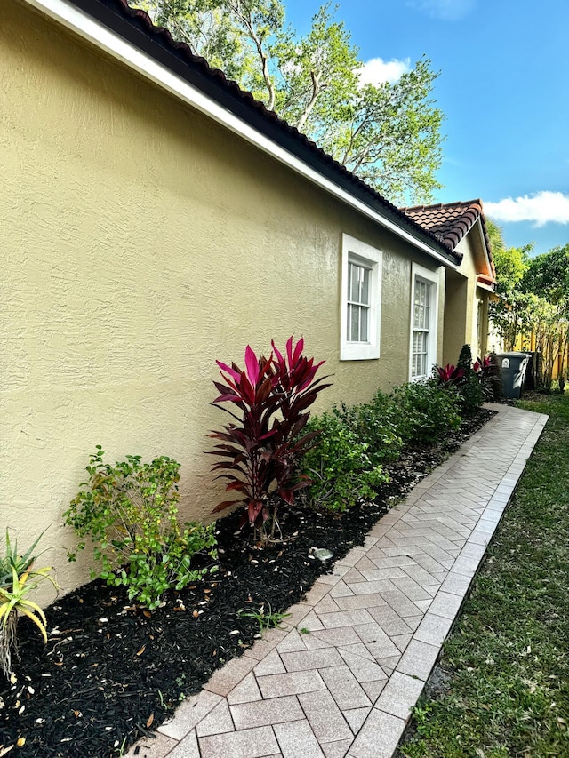 view of property exterior featuring a tile roof, fence, and stucco siding