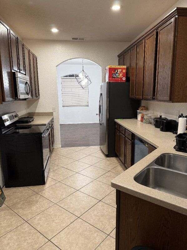 kitchen featuring electric range, arched walkways, stainless steel microwave, dark brown cabinets, and a sink