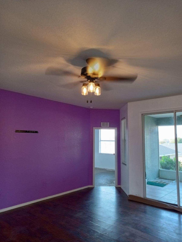 unfurnished room with a ceiling fan, dark wood-style flooring, visible vents, and baseboards