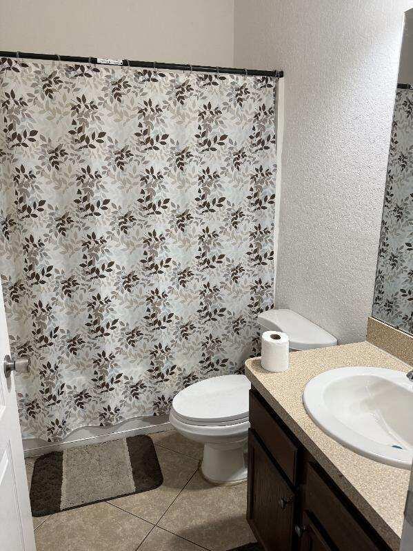 full bathroom featuring a textured wall, curtained shower, toilet, vanity, and tile patterned floors