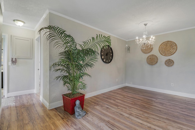 unfurnished room with an inviting chandelier, crown molding, baseboards, and wood finished floors