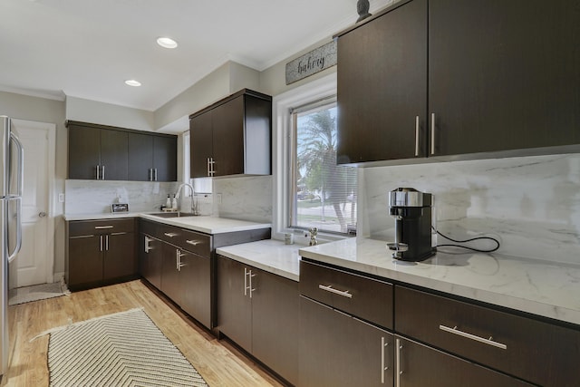 kitchen with tasteful backsplash, ornamental molding, light wood-style floors, a sink, and dark brown cabinets