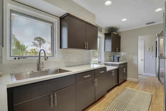 kitchen with visible vents, decorative backsplash, light wood-style flooring, light countertops, and a sink