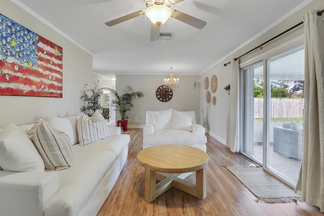 living room featuring ceiling fan with notable chandelier, visible vents, baseboards, light wood finished floors, and crown molding