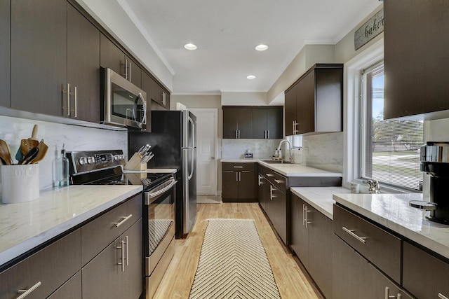 kitchen featuring dark brown cabinetry, tasteful backsplash, stainless steel appliances, light wood-type flooring, and a sink