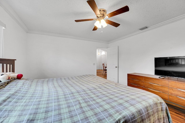 bedroom with crown molding, visible vents, ceiling fan, a textured ceiling, and wood finished floors