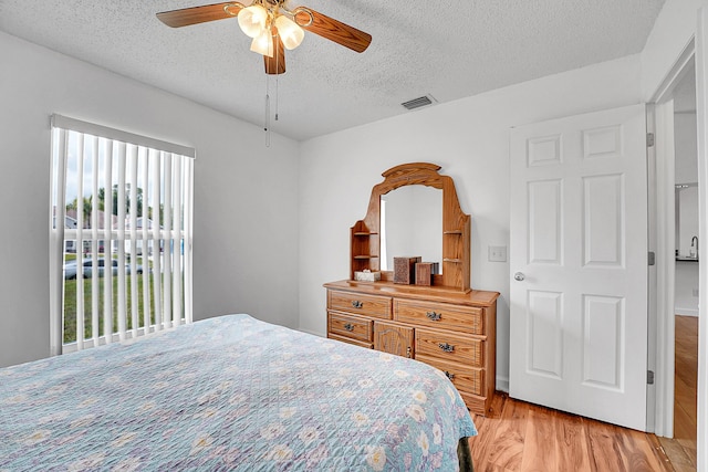 bedroom with light wood-style floors, a ceiling fan, visible vents, and a textured ceiling