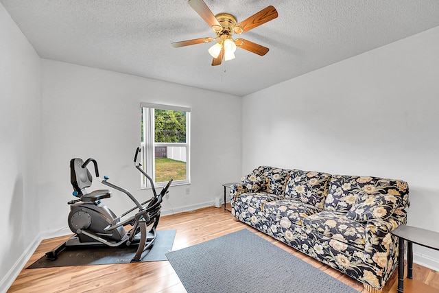 workout room with light wood-type flooring, a textured ceiling, and baseboards