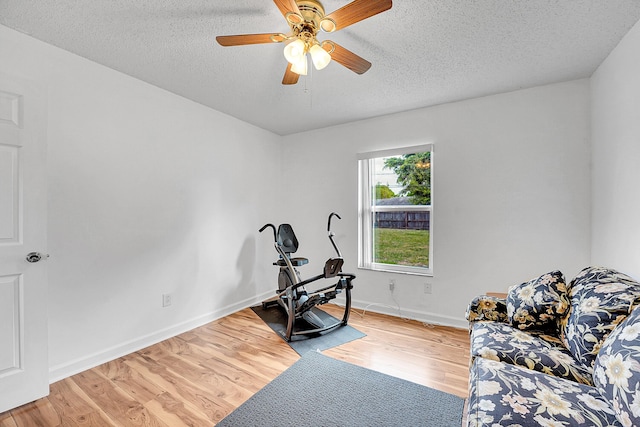 workout room with a ceiling fan, a textured ceiling, baseboards, and wood finished floors