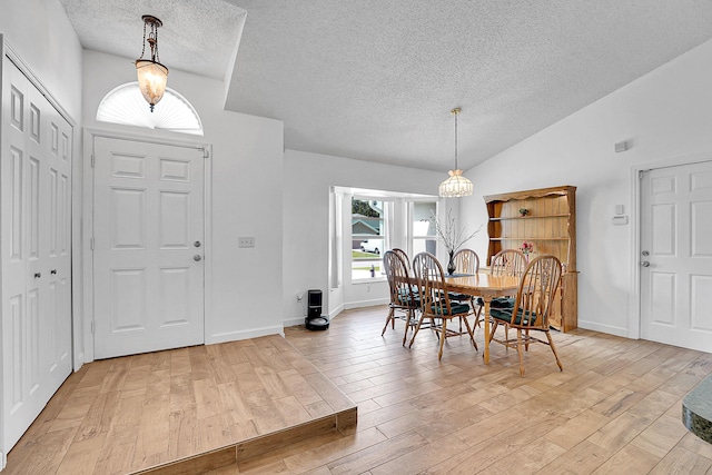 dining space featuring lofted ceiling, light wood-style floors, baseboards, and a textured ceiling