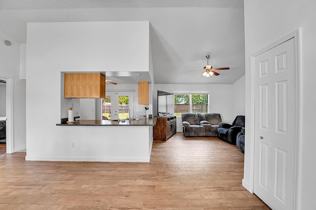 kitchen with light wood finished floors, dark countertops, a ceiling fan, open floor plan, and a sink