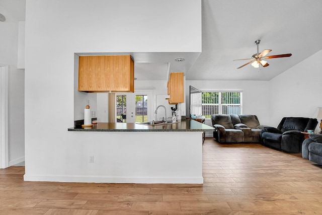 kitchen with a ceiling fan, dark countertops, wood finished floors, vaulted ceiling, and a sink