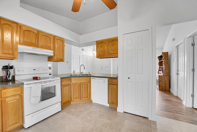 kitchen featuring white appliances, light tile patterned floors, dark countertops, under cabinet range hood, and a sink