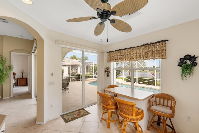 dining area with baseboards, arched walkways, a sunroom, ceiling fan, and light tile patterned flooring