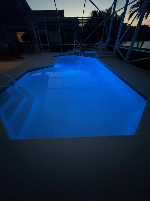 pool at dusk featuring glass enclosure, a patio, and a pool with connected hot tub