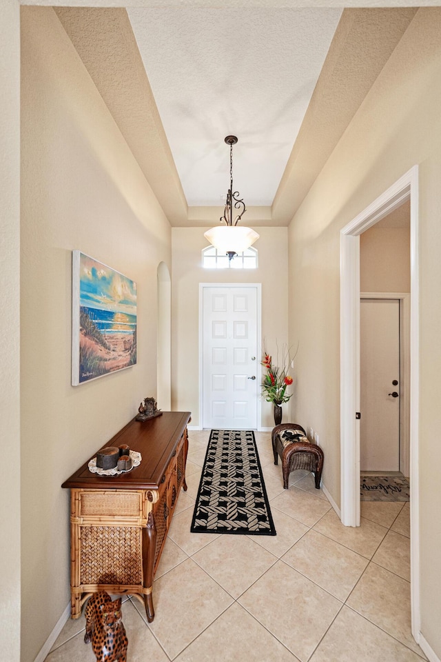 foyer featuring baseboards, a tray ceiling, arched walkways, and light tile patterned flooring