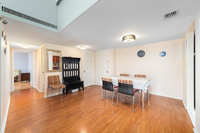 dining area featuring light wood-style floors, visible vents, a textured ceiling, and baseboards