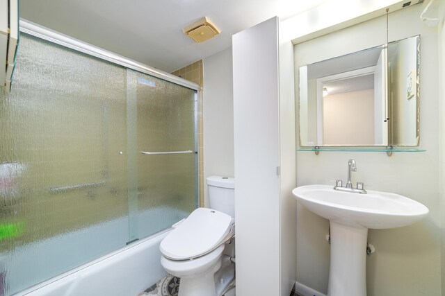 bathroom with toilet, enclosed tub / shower combo, and a sink