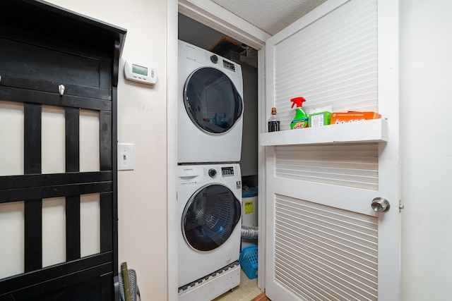 clothes washing area featuring laundry area, a textured ceiling, and stacked washer / dryer