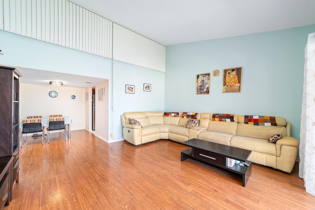 living area with light wood-style floors, a towering ceiling, and baseboards