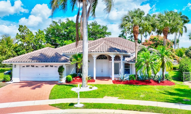 mediterranean / spanish house with a tile roof, stucco siding, a garage, driveway, and a front lawn